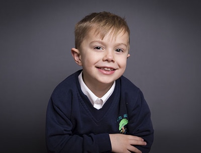 School photograph of child folding arms and leaning on table 